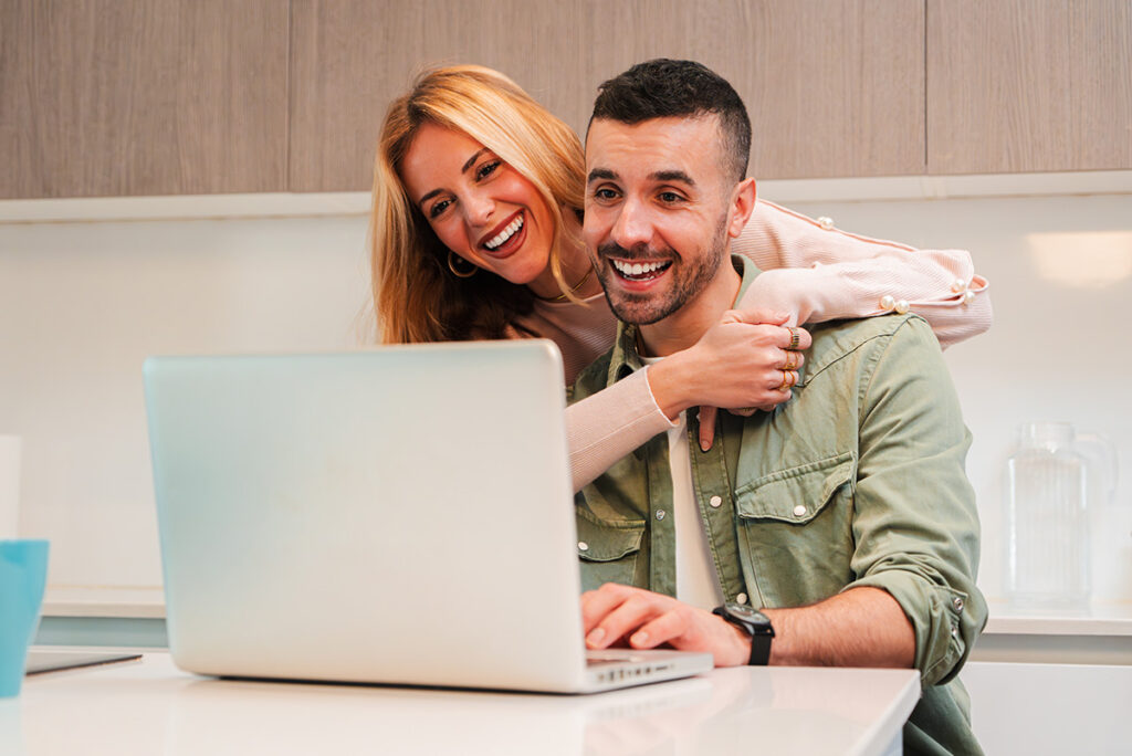 Couple québécois souriant consultant une demande de prêt rapide en ligne sur un ordinateur portable.