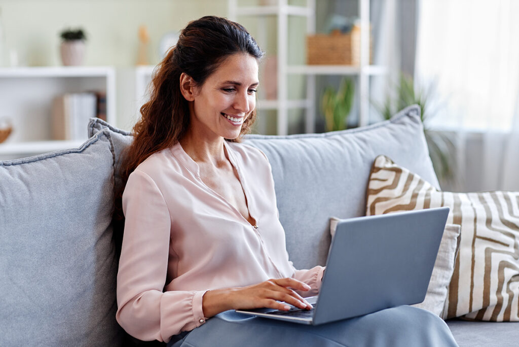 Femme souriante utilisant un ordinateur portable pour trouver un prêteur en quelques minutes en ligne.